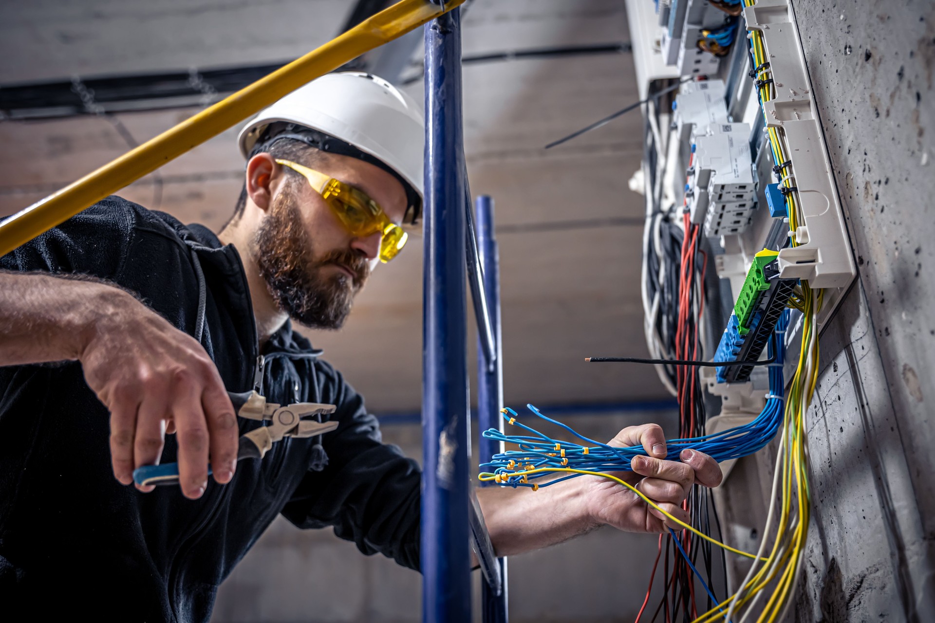 A male electrician works in a switchboard with an electrical connecting cable. A male electrician works in a switchboard with an electrical connecting cable.